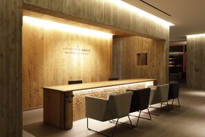 A reception area with a wooden reception desk and chairs, a textured wall with a logo, and a modern interior design. - Regina Resort Kyukaruizawa (Karuizawa)
