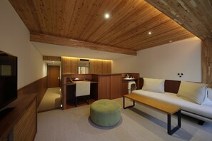 A modern living room with a wooden ceiling, a sofa, a coffee table, a TV, and a kitchen area with a sink and cabinets. - Regina Resort Kyukaruizawa (Karuizawa)