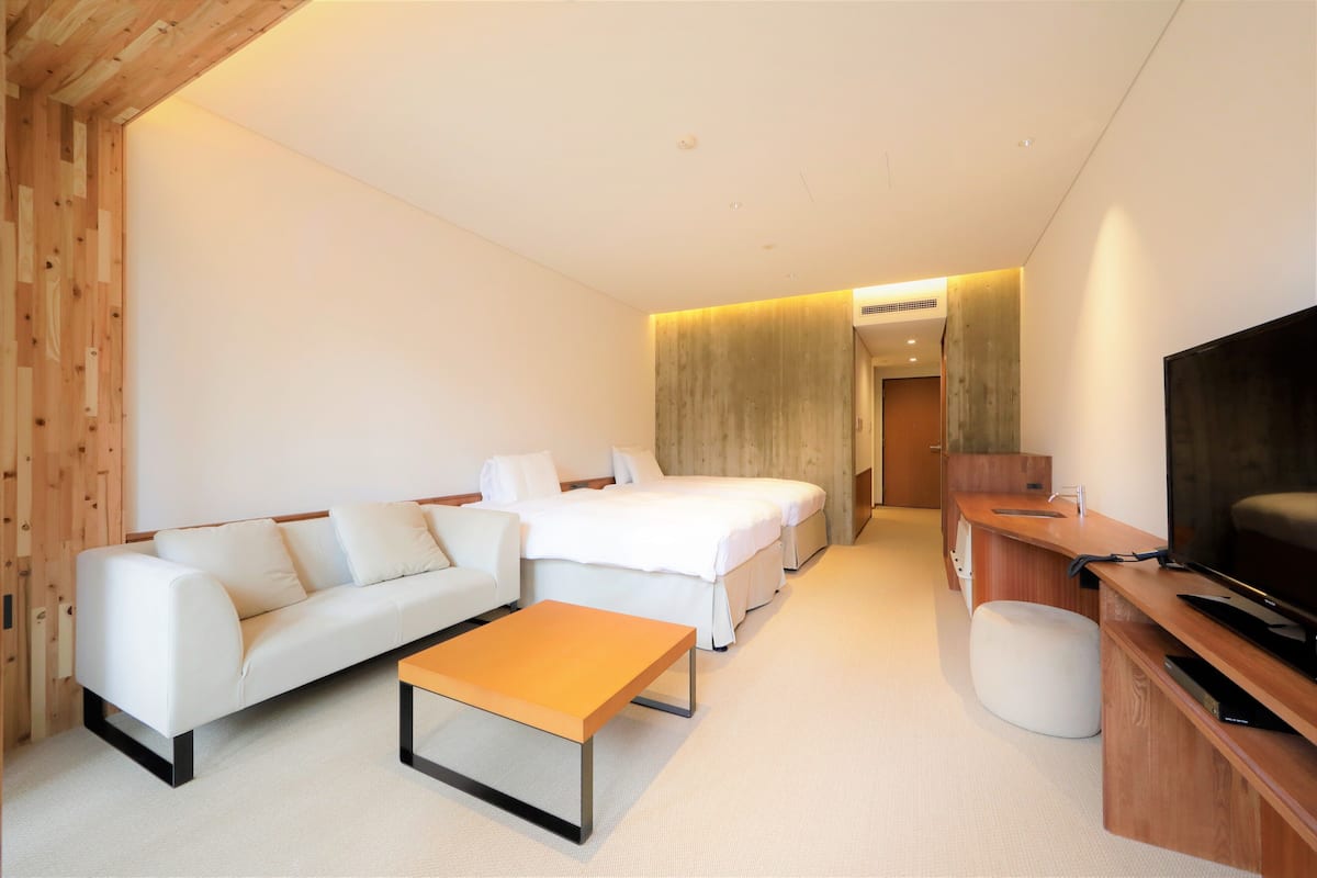 A modern hotel room with a sofa, a bed, a wooden desk, and a television.