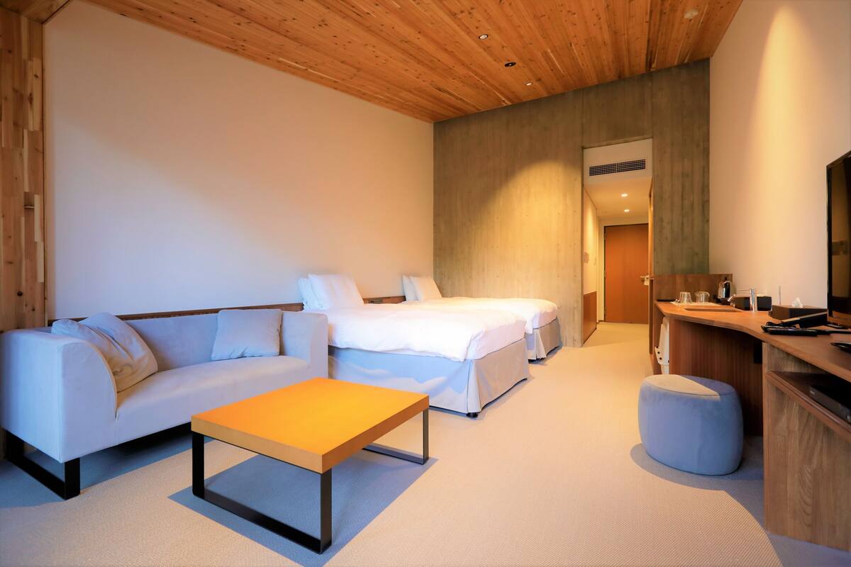 A modern hotel room with a wooden ceiling, a sofa, a bed, a small table, and a TV.