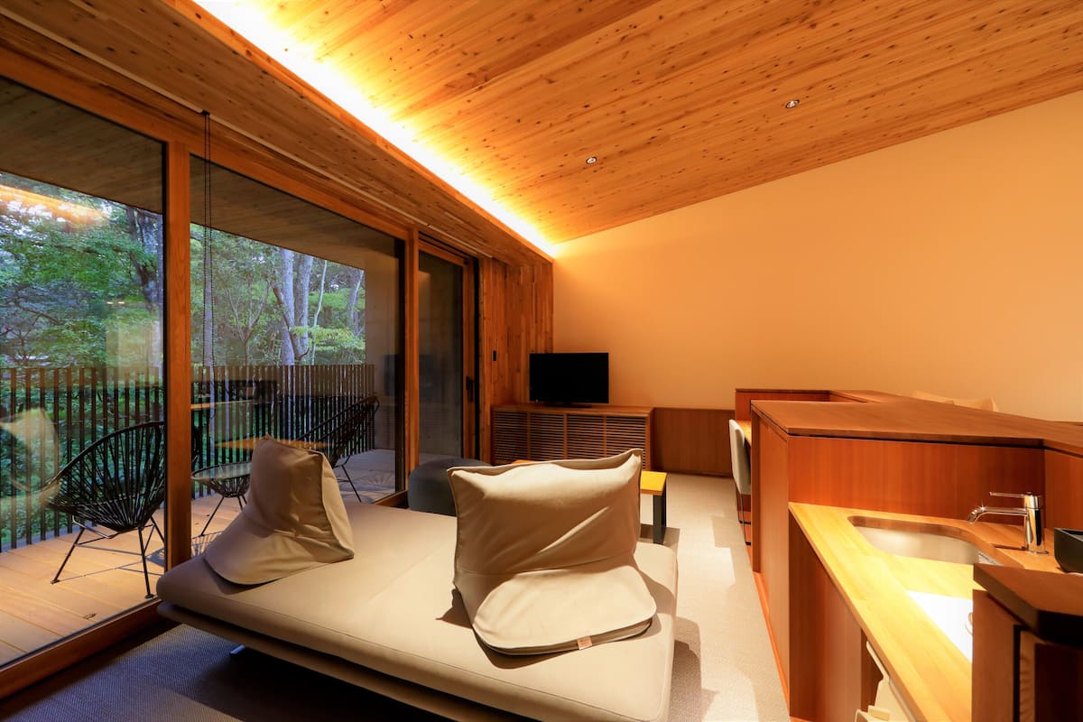 A modern room with a wooden ceiling, a sofa with cushions, a TV, and a wooden counter with a sink.