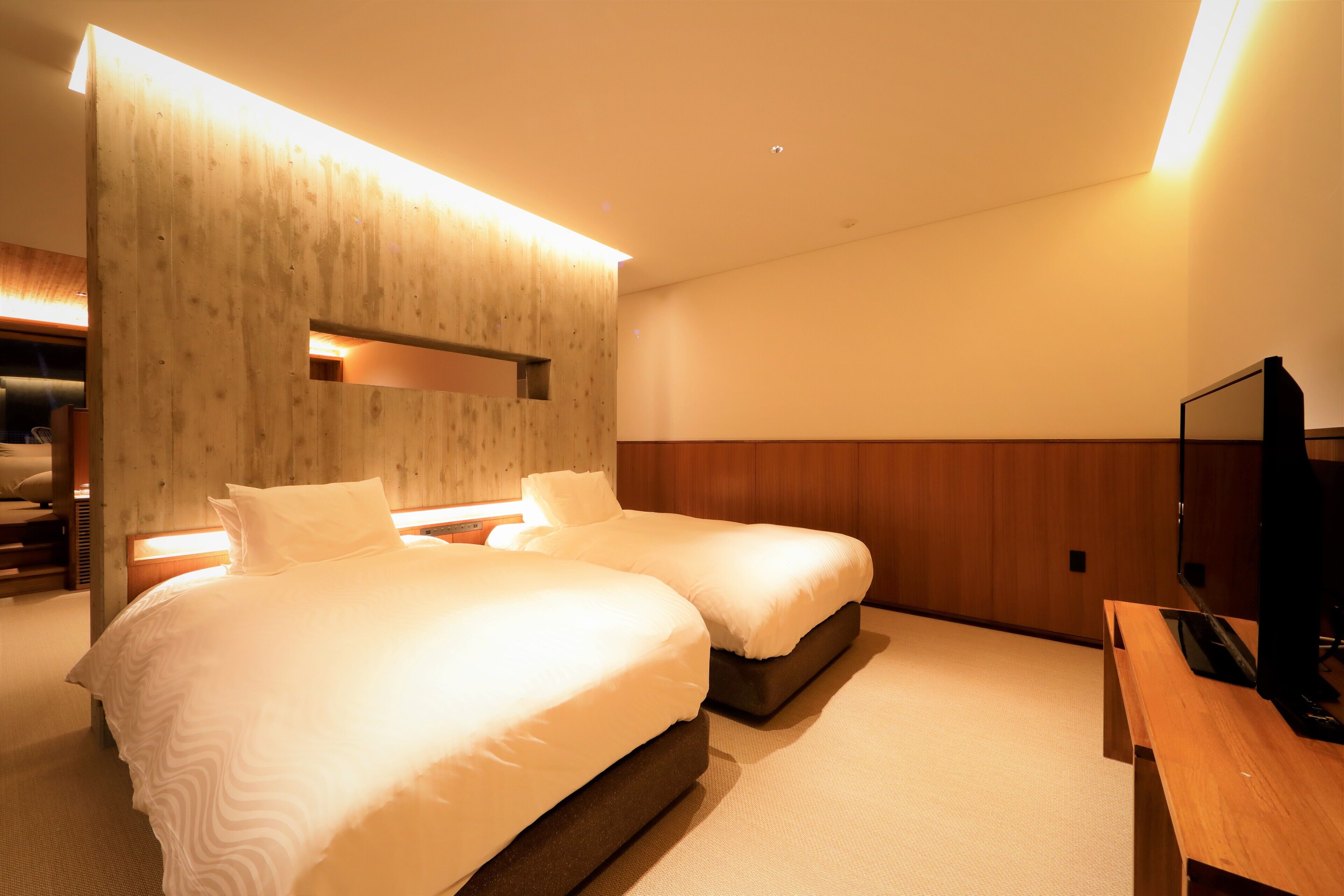 A hotel room with two beds, a wooden accent wall, a flat-screen TV, and a wooden desk.