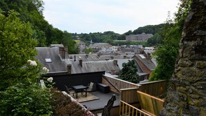 A rooftop patio with outdoor furniture, a stone wall, and a view of a town with buildings and trees. - Le Toit de Dinant - Esc’Appart (Dinant)