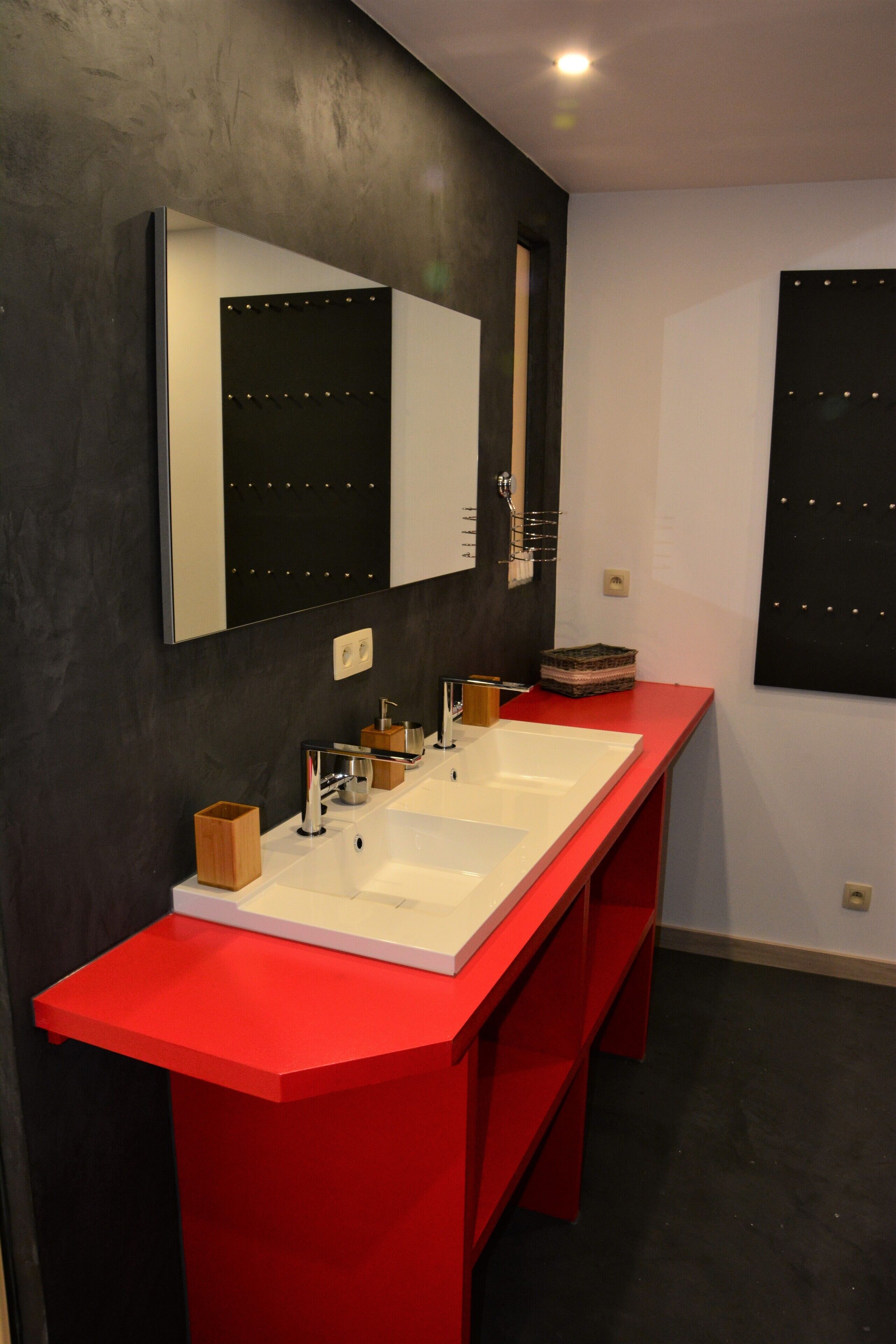 A modern bathroom with a red vanity, two sinks, and a large mirror.