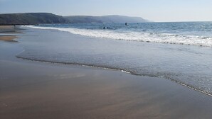 Ein Strand mit klarem Himmel, Wellen und sanften Hügeln im Hintergrund.