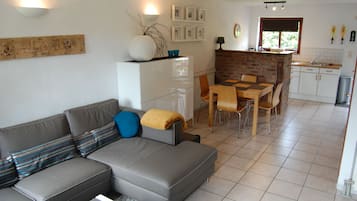 A modern living room with a grey sofa, a coffee table, and a dining area with wooden chairs and a small table.