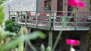 Un bâtiment rustique avec une façade en pierre et un pont en bois menant à un balcon agrémenté de chaises rouges.