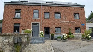 Un bâtiment en briques rouges, avec une porte et des fenêtres grises, un mur de pierre orné de boîtes aux lettres et des plantes en pot.
