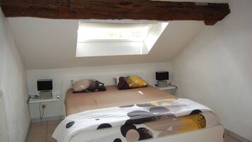 Een slaapkamer met een schuine kap, dakraam, een bed met een decoratieve spreidek, twee nachtkastjes met lampen en een aan de muur bevestigde televisie.