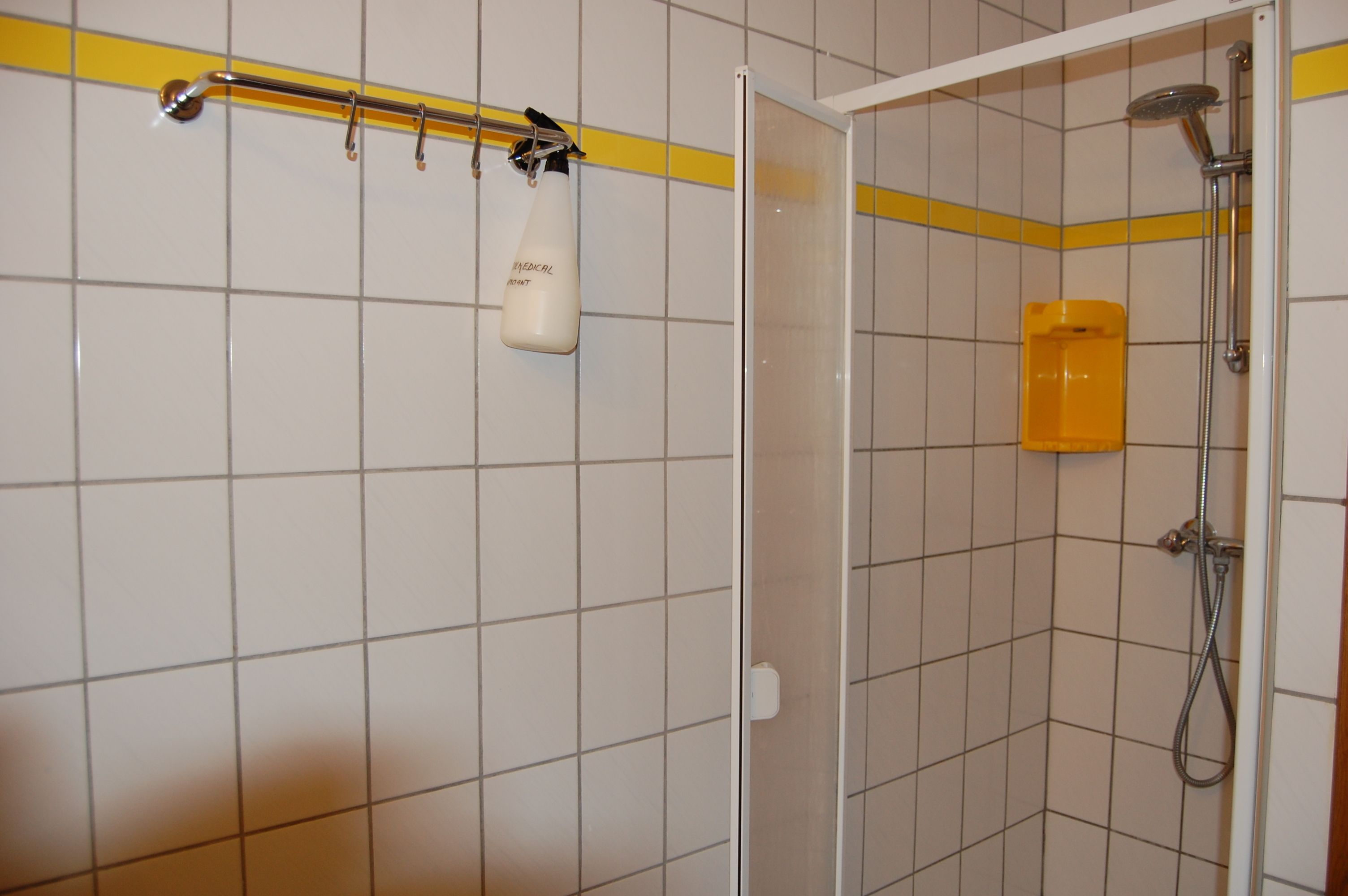 Un área de ducha con puerta de vidrio, una franja amarilla en la pared y un botiquín médico blanco colgado en el marco de la puerta.