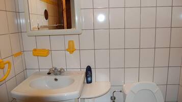 Ein Badezimmer mit einem weißen Waschbecken, einem Spiegel, einer Toilette und einem gelben Seifenspender.