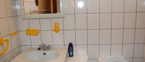 A bathroom with a white sink, a mirror, a toilet, and a yellow soap dispenser.
