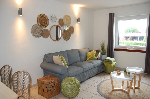 A modern living room with a grey sofa, round mirrors, and a large window with curtains.