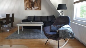 A modern living room with a wooden floor, a white sofa, a black rocking chair, a coffee table, and a large painting of lions. - Apartment / Monteurzimmer (Seesen)