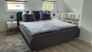 A bedroom with a large bed, two bedside tables, a nightstand, a window with blinds, and a view of greenery outside. - Apartment / Monteurzimmer (Seesen)