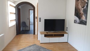 A modern living room with a flat-screen TV on a white entertainment unit, a grey rug on the floor, and a lion painting on the wall. - Apartment / Monteurzimmer (Seesen)
