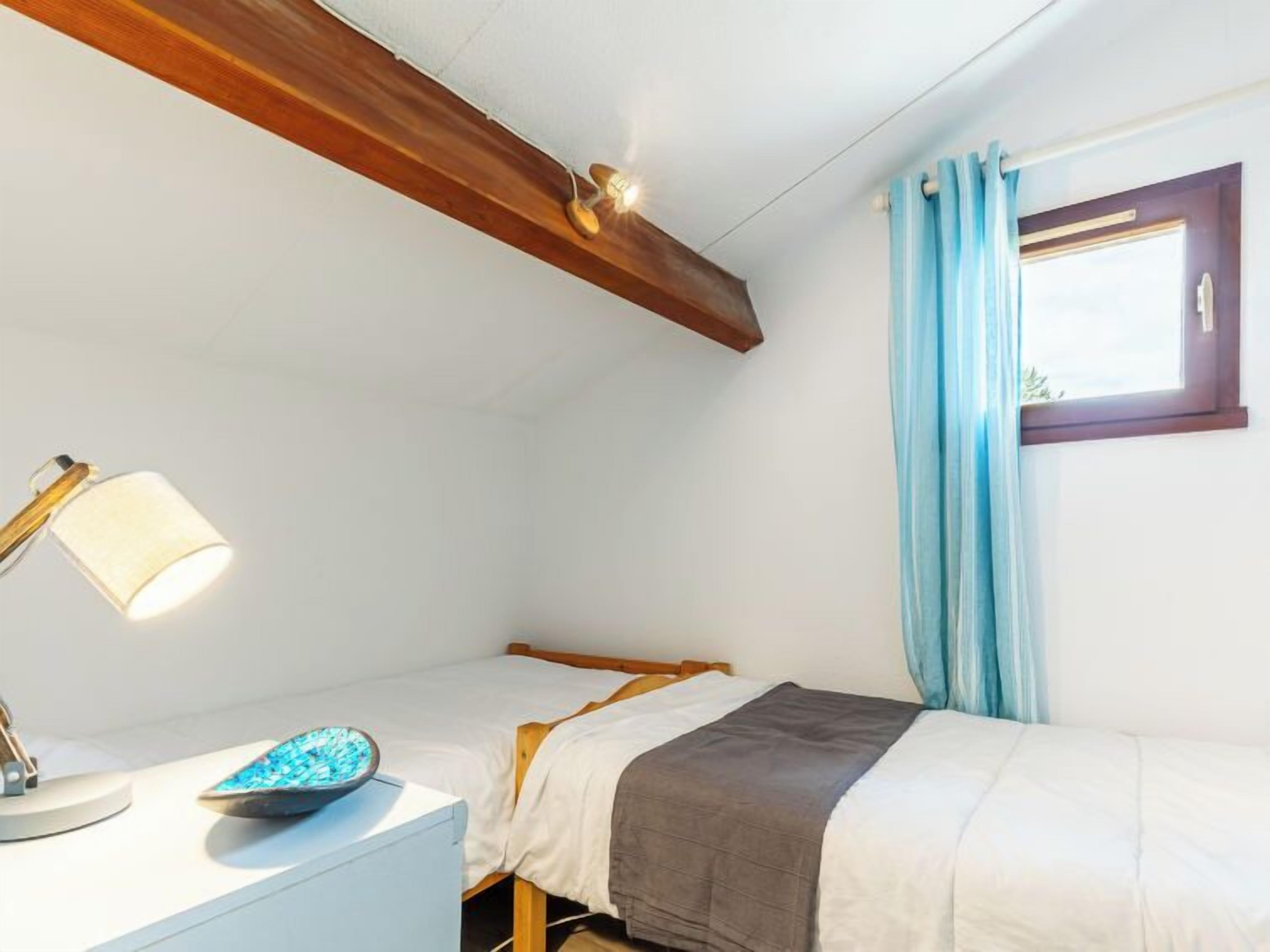 Een kleine, netjes ingerichte slaapkamer met een enkel bed, een nachtkastje met lamp en een raam met gordijnen.