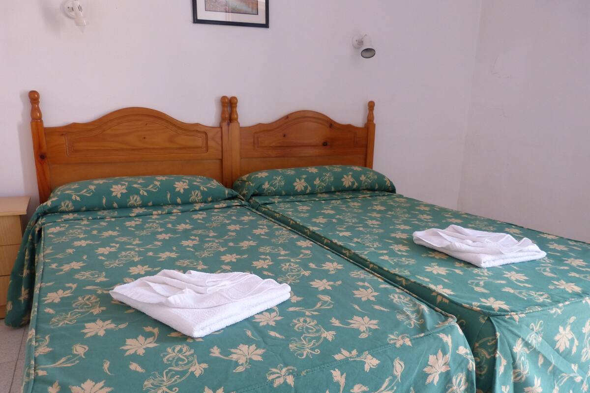 Una cama doble con ropa de cama floral, dos almohadas y toallas dobladas a cada lado.