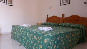 Een hotelkamer met een tweepersoonsbed, een bedspreider met groene bloemenprint en netjes opgevouwen witte handdoeken op het bed.