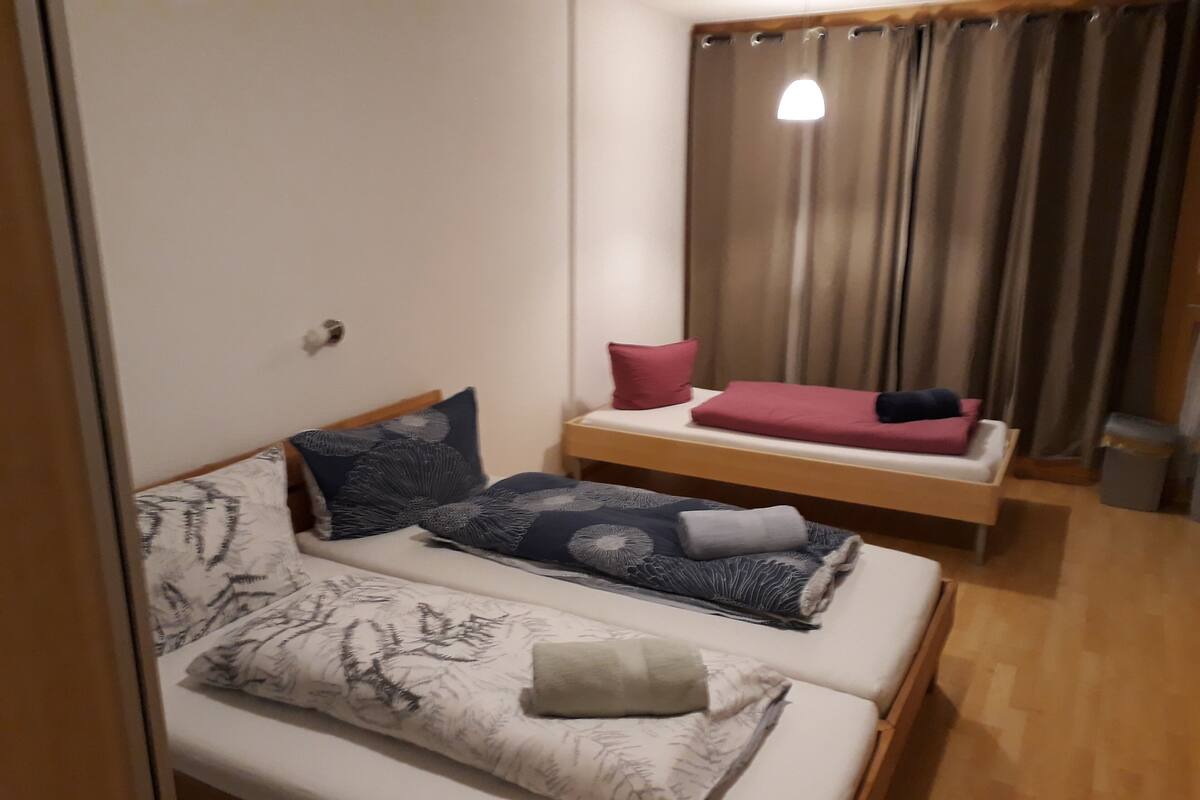 A small, cozy room with two beds, a bedside table, and a curtain.