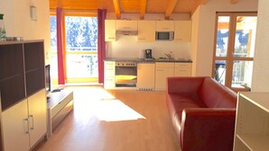 Ein kleiner Wohnraum mit Küchenzeile, einem roten Sofa und einem Fernseher.