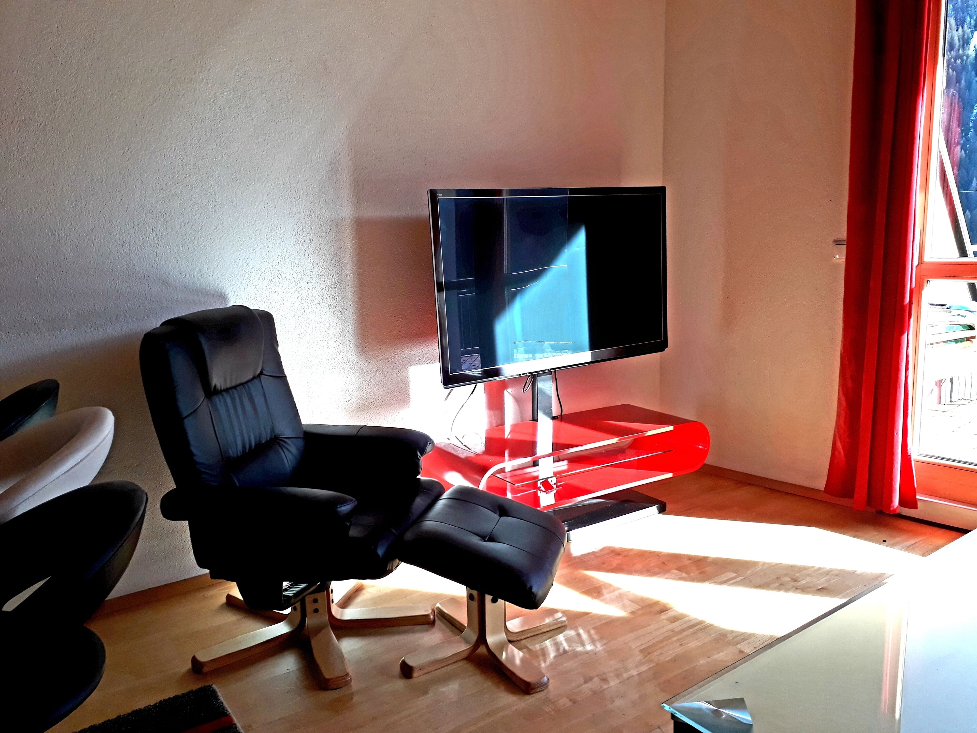 Ein modernes Wohnzimmer mit einem schwarzen Ledersessel, einer roten Unterhaltungsanlage und einem flachbildfernseher an der Wand.