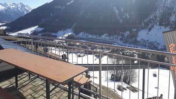 Blick von einem Balkon auf eine verschneite Berglandschaft, in der Ferne eine Seilbahn.