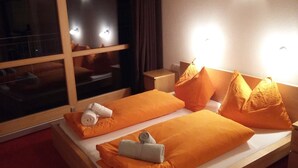 Ein Hotelzimmer mit zwei Betten, jeweils mit orangefarbener Bettwäsche und Kissen, sowie einem Fenster mit Vorhängen.