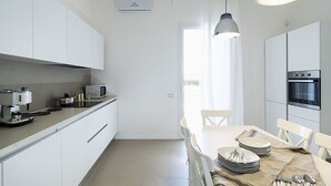 Een moderne keuken met witte kasten, een inbouwoven, een koffieapparaat en een eethoek met een tafel voor vier personen.