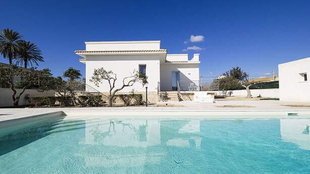 Een moderne villa met een zwembad, witte muren en een helderblauwe lucht.