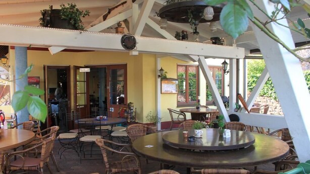 An outdoor seating area with wicker furniture and a round table, surrounded by potted plants and a white structure with beams. - Hotel Krone Kappel (Kappel-Grafenhausen)
