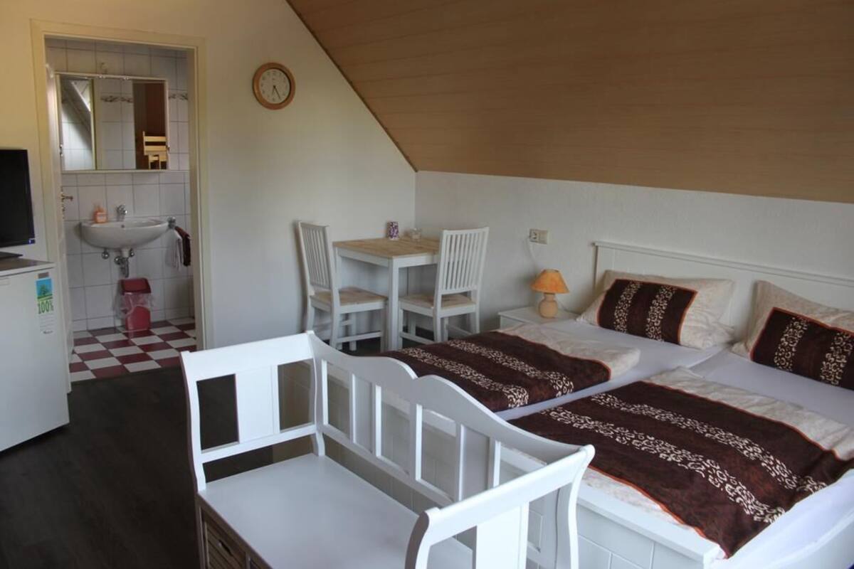Une chambre à coucher comprenant un lit, un bureau, une chaise, une petite table, un lavabo et un miroir.