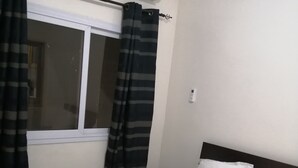Hotelkamer met een bed, een raam met gordijnen, een airconditioning en een nachtkastje met een kussen.