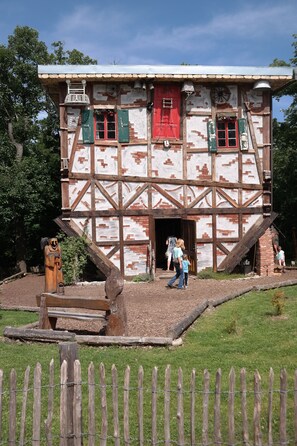 Un bâtiment traditionnel à colombages, avec une porte rouge et des volets verts, un escalier en bois et un petit jardin.