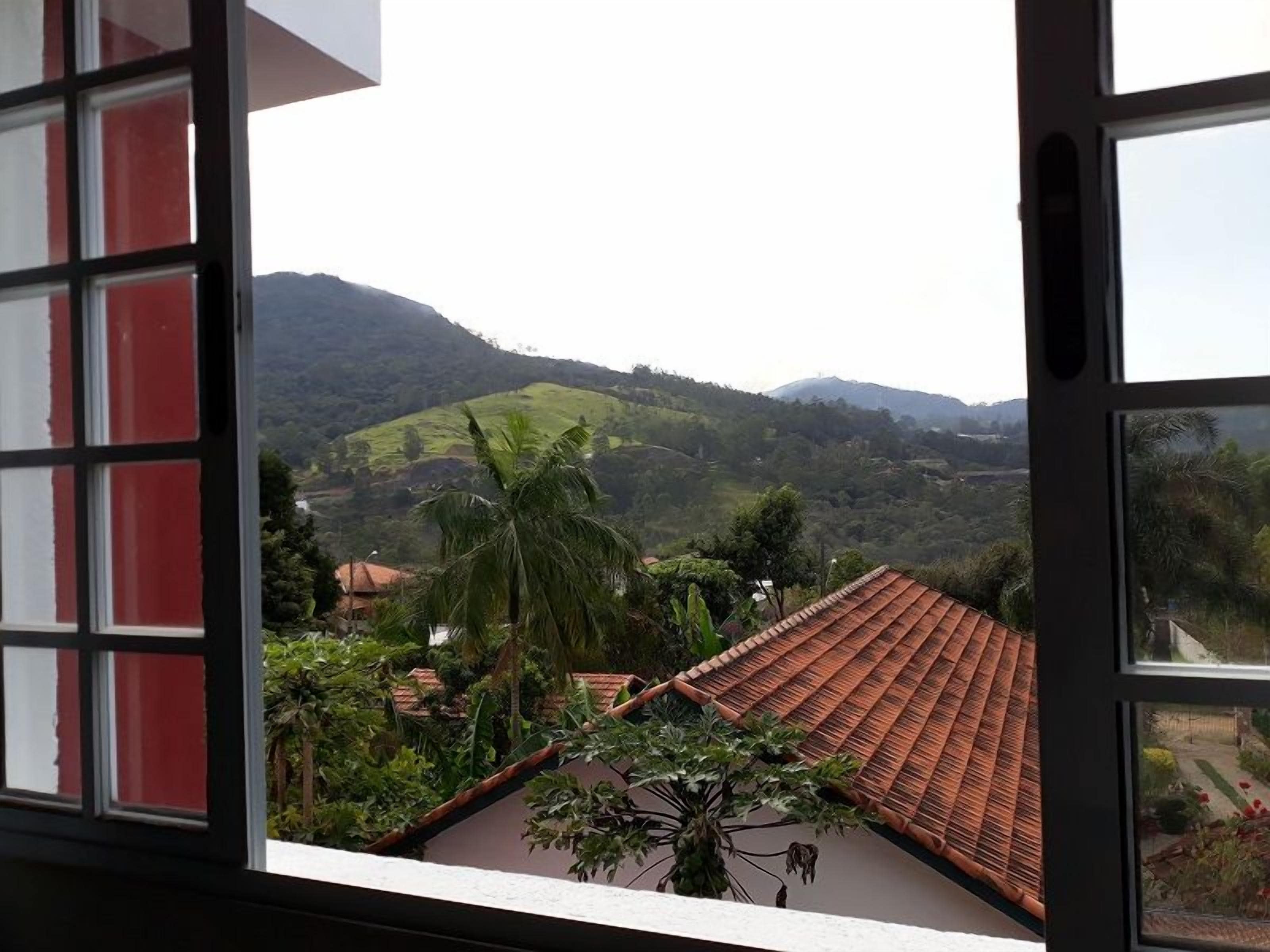 Una vista dalla finestra con cornice rossa, su una casa con tetto in tegole rosse e un paesaggio verdeggiante con colline sullo sfondo.