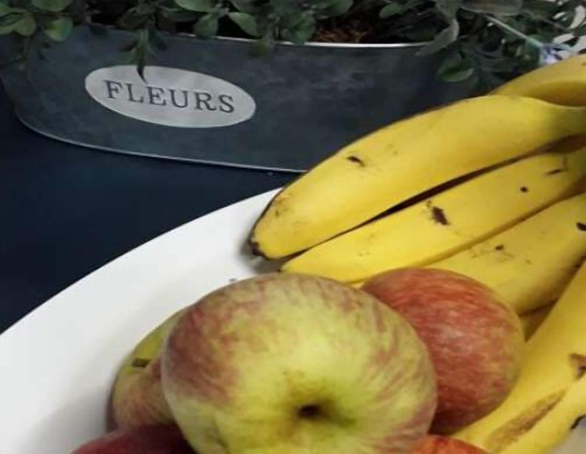 Ein Teller mit Bananen und Äpfeln auf einem Tisch.