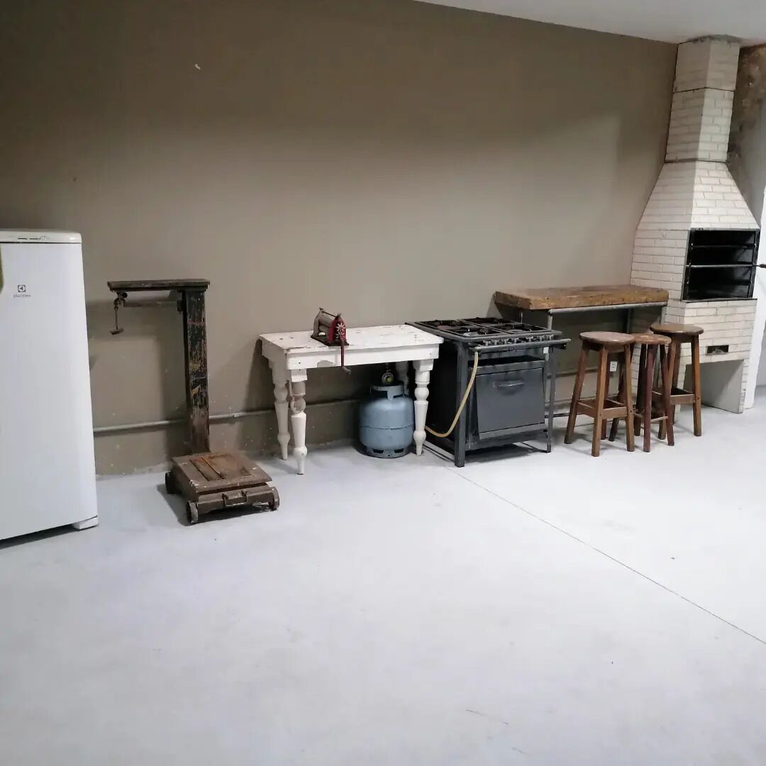 A kitchen with a gas stove, a brick oven, a small refrigerator, a wooden table, and a gas cylinder.