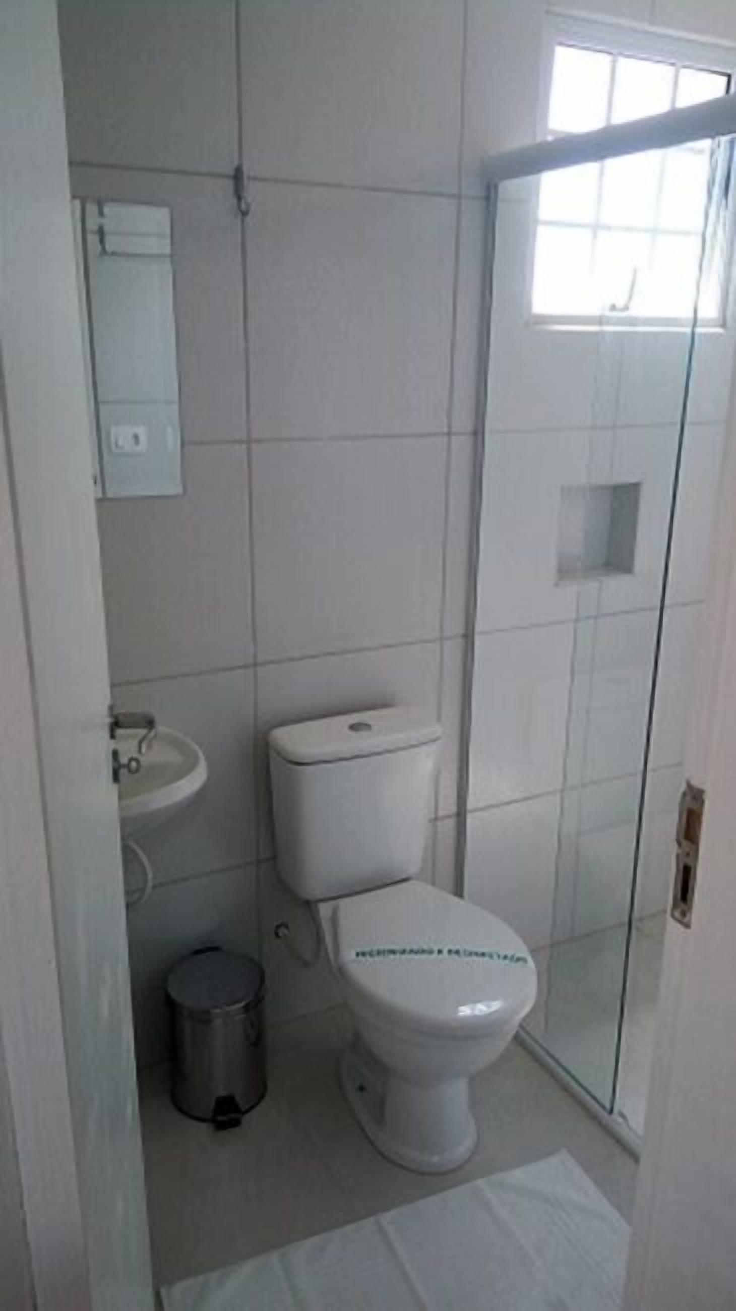 A bathroom with a toilet, sink, and a trash bin.