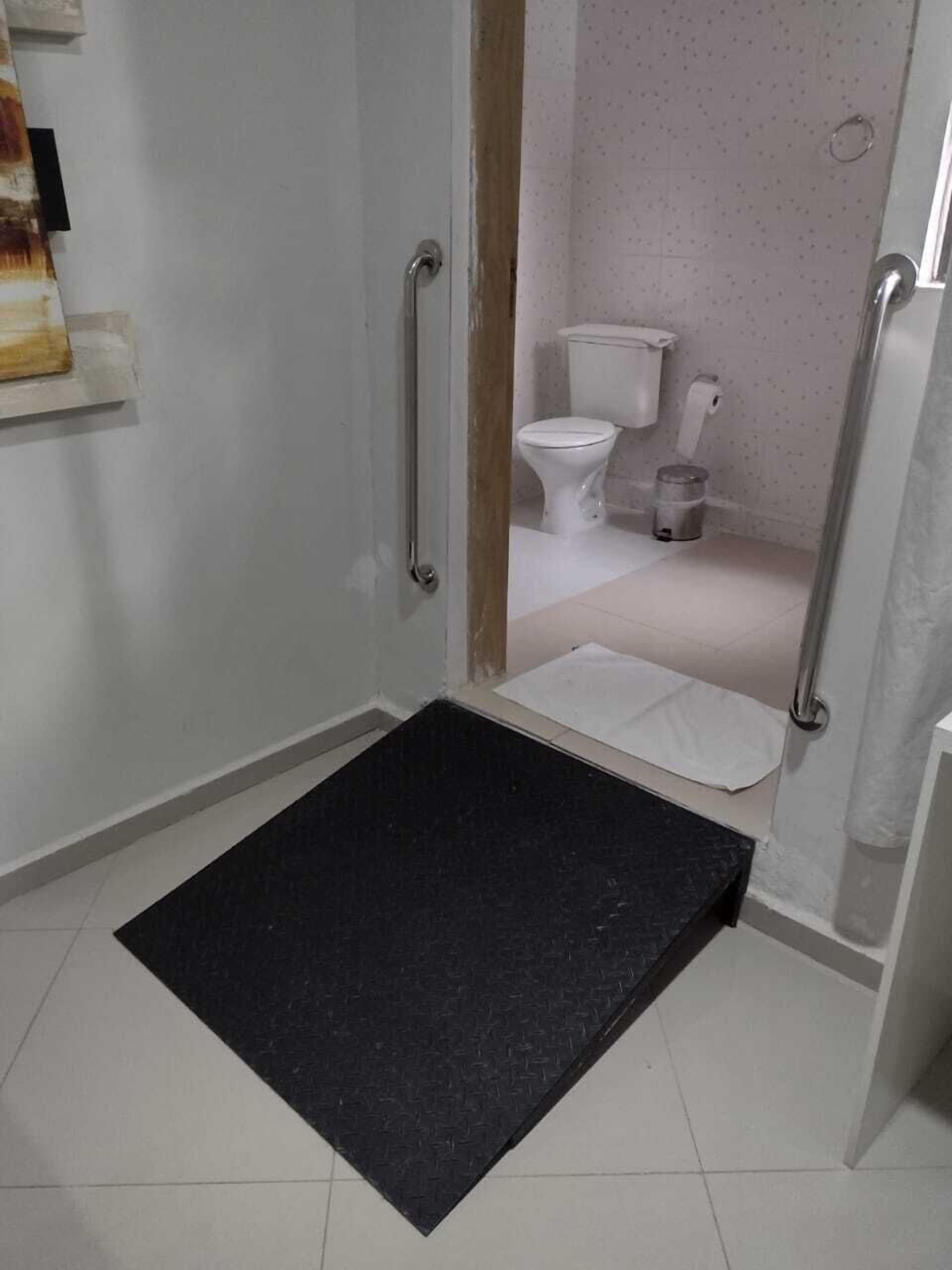 A bathroom with a white toilet, a trash bin, and a shower area with a black mat.