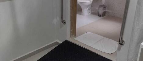 A bathroom with a white toilet, a trash bin, and a shower area with a black mat.