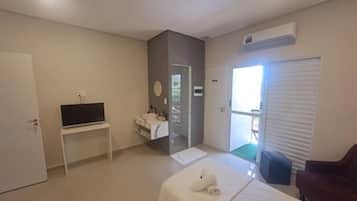 Habitación de hotel con cama, televisor sobre un mueble, baño con lavamanos y puerta corredera al exterior.