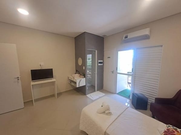 A hotel room with a bed, a TV on a stand, a bathroom with a sink, and a sliding door to the outside. - Pousada Top (Mairipora)