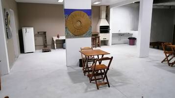 Una habitación amplia con comedor que incluye una mesa y sillas de madera, un refrigerador blanco, zona de cocina con estufa y lavaplatos, y un elemento decorativo en la pared.