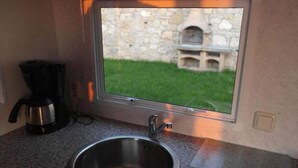 A kitchen with a stainless steel sink, a coffee maker, and a window overlooking a stone wall and a grassy yard. - Agricampeggio Agri-camping Relax (Brenzone sul Garda)