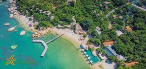 Ein Luftbild eines Küstenresorts mit Strand, klarem Wasser, einem hölzernen Steg und strohgedeckten Gebäuden.