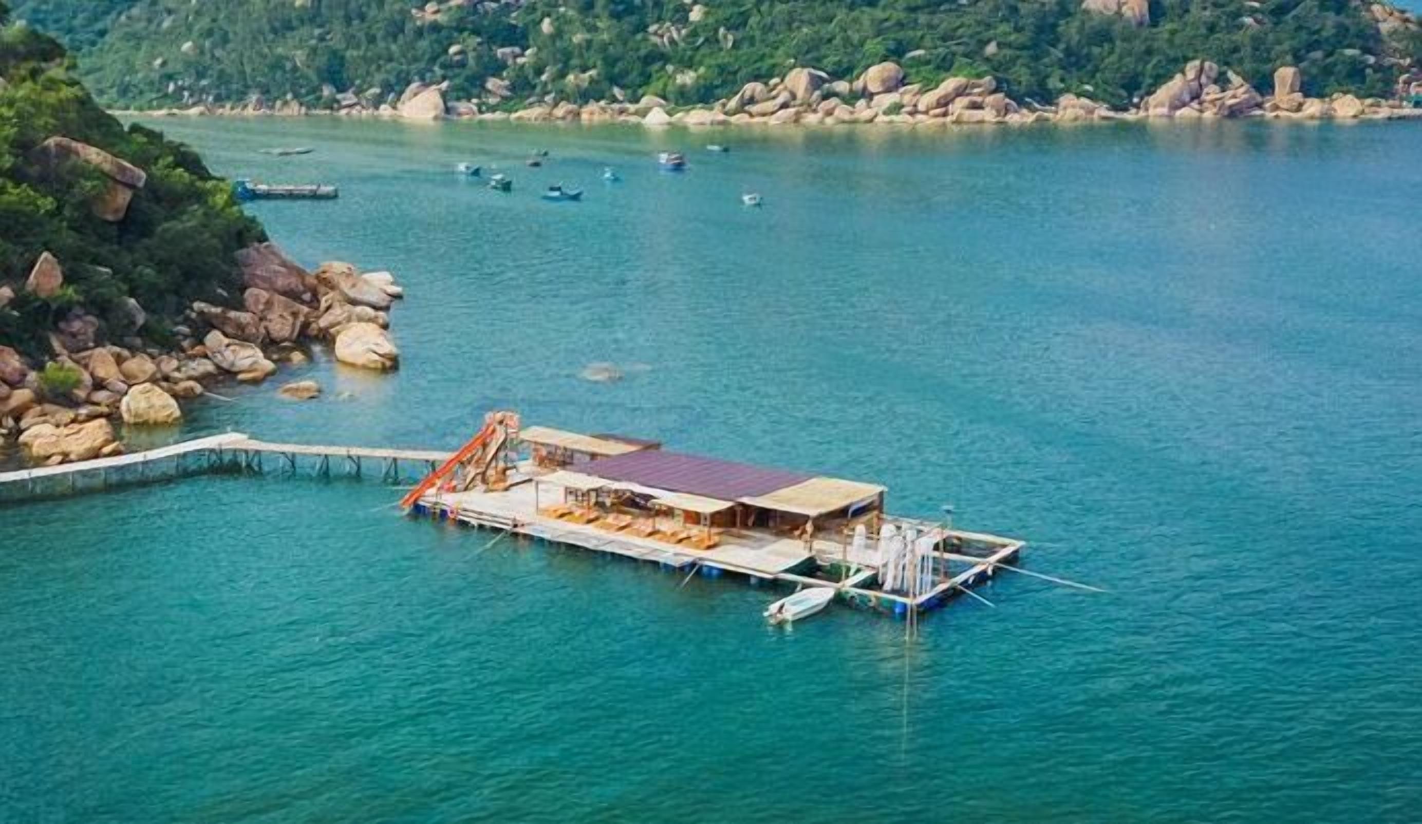 A floating structure with a covered area and a dock, surrounded by calm water and rocky terrain.