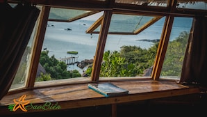 A view from a window with a wooden frame and a thatched roof, overlooking a body of water with boats and greenery. - Sao Bien Cam Ranh (Nam Cam Ranh)