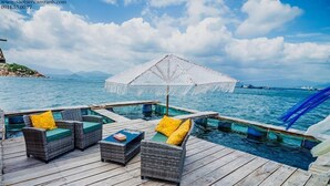 A wooden deck with wicker furniture and a white umbrella. - Sao Bien Cam Ranh (Nam Cam Ranh)