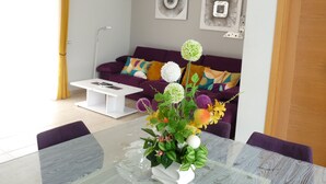 Un salon moderne avec une table à manger en verre, un canapé violet et une table basse blanche.