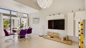 Un salon moderne avec une table à manger en verre, des chaises violettes, un grand téléviseur à écran plat et une décoration minimaliste.